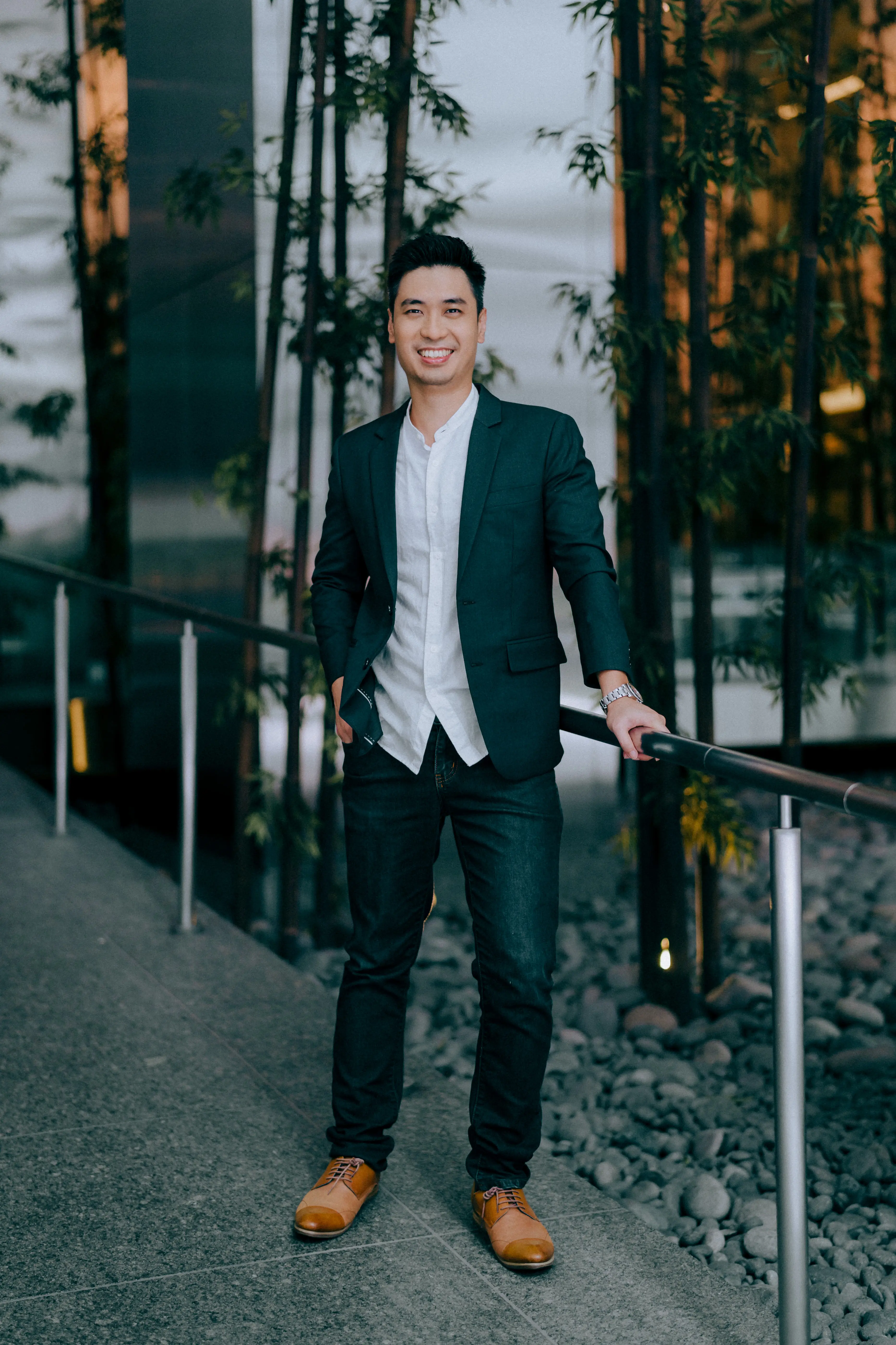 Ling Chun Wei standing outdoors beside a railing, with bamboo and an office building behind him