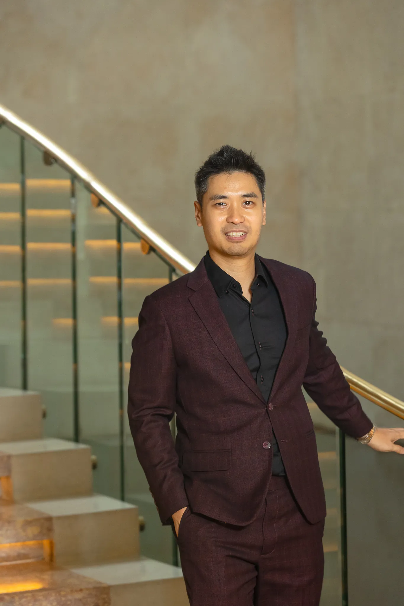 Ling Chun Wei in a dark suit, standing beside a lit staircase